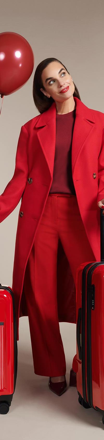 A woman in a red coat standing with two red Briggs & Riley expandable spinner suitcases