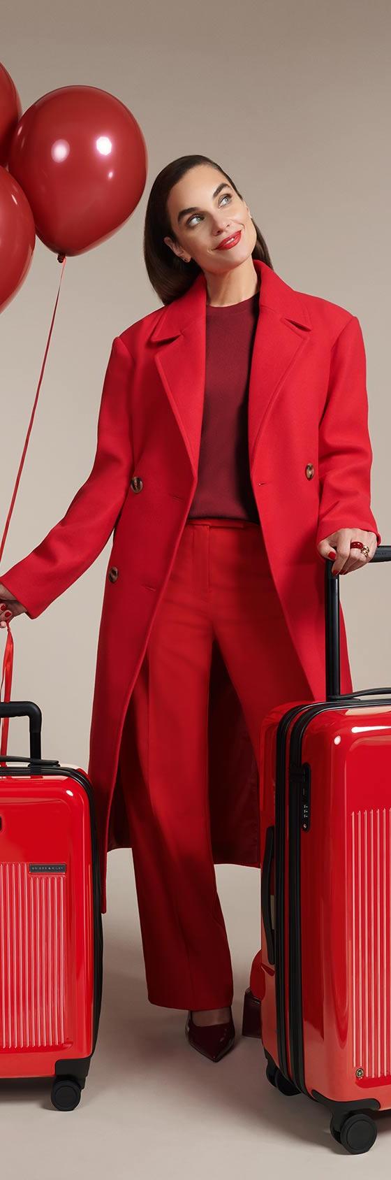 A woman in a red coat standing with two red Briggs & Riley expandable spinner suitcases