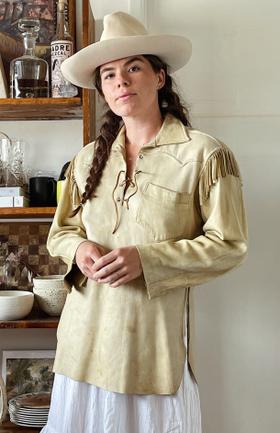 A woman wearing a cream fringed buckskin western shirt and wide-brim felt hat