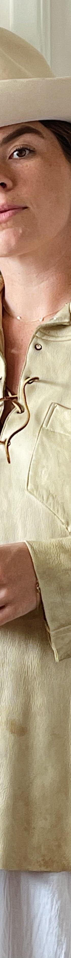 A woman wearing a cream fringed buckskin western shirt and wide-brim felt hat