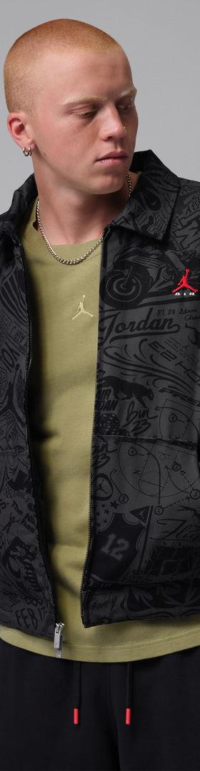 A man wearing a black all-over print Jordan coach jacket over an olive tee