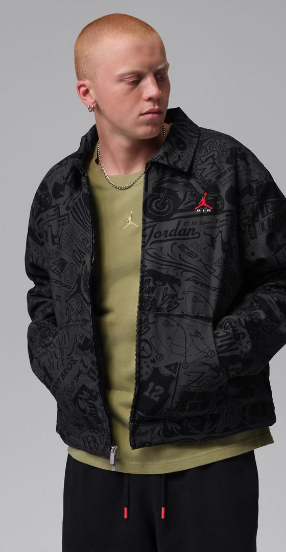 A man wearing a black all-over print Jordan coach jacket over an olive tee