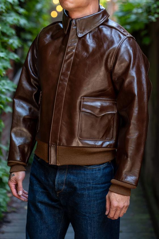 A man wearing a brown Buzz Rickson's A-2 leather flight jacket with dark indigo jeans