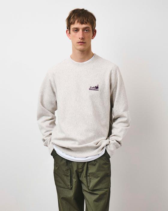 A man wearing an oatmeal Café Mountain sweatshirt with olive ripstop trousers