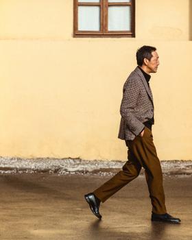 A man walking in a checked Camoshita United Arrows sport coat, black turtleneck and tobacco brown trousers