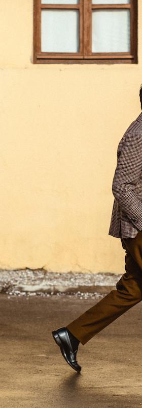 A man walking in a checked Camoshita United Arrows sport coat, black turtleneck and tobacco brown trousers