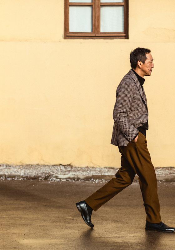 A man walking in a checked Camoshita United Arrows sport coat, black turtleneck and tobacco brown trousers