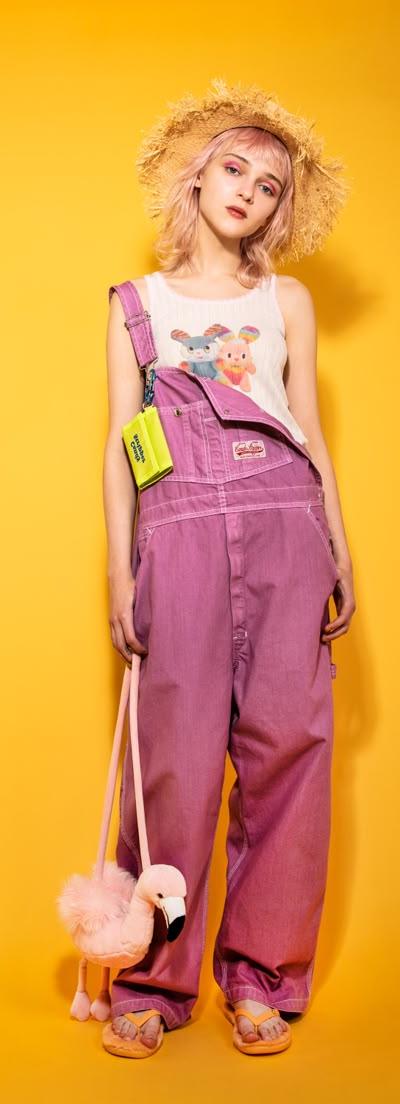 A woman wearing pink Candy Stripper overalls with a graphic tank top and straw hat