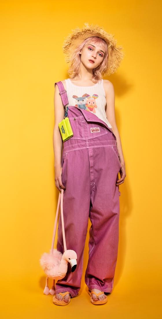 A woman wearing pink Candy Stripper overalls with a graphic tank top and straw hat