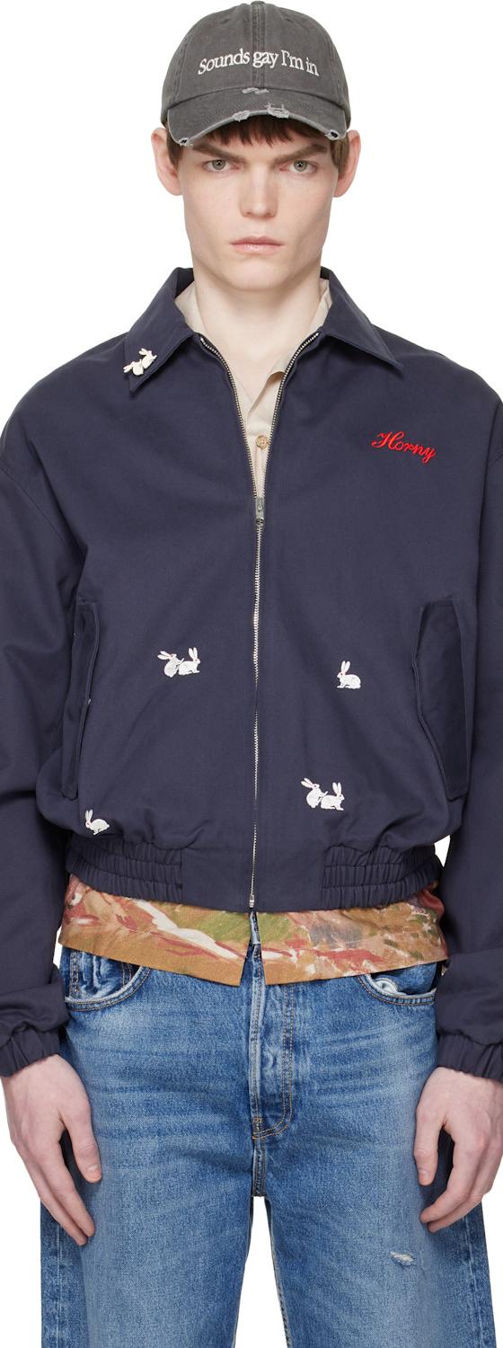 A man wearing a navy Carne Bollente embroidered bomber jacket and cap