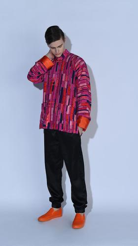 A man wearing a bold pink and purple patterned oversized jacket with black trousers and orange sneakers