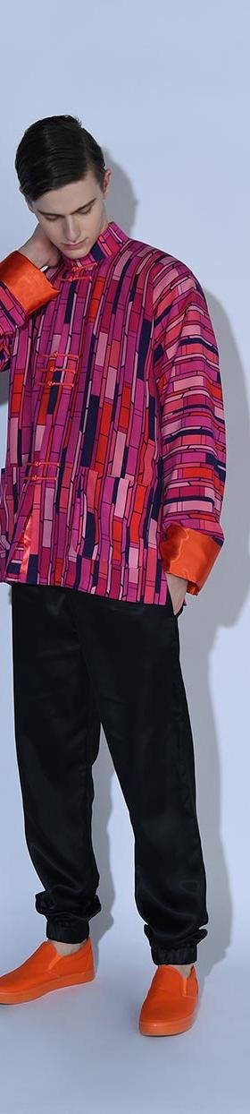 A man wearing a bold pink and purple patterned oversized jacket with black trousers and orange sneakers