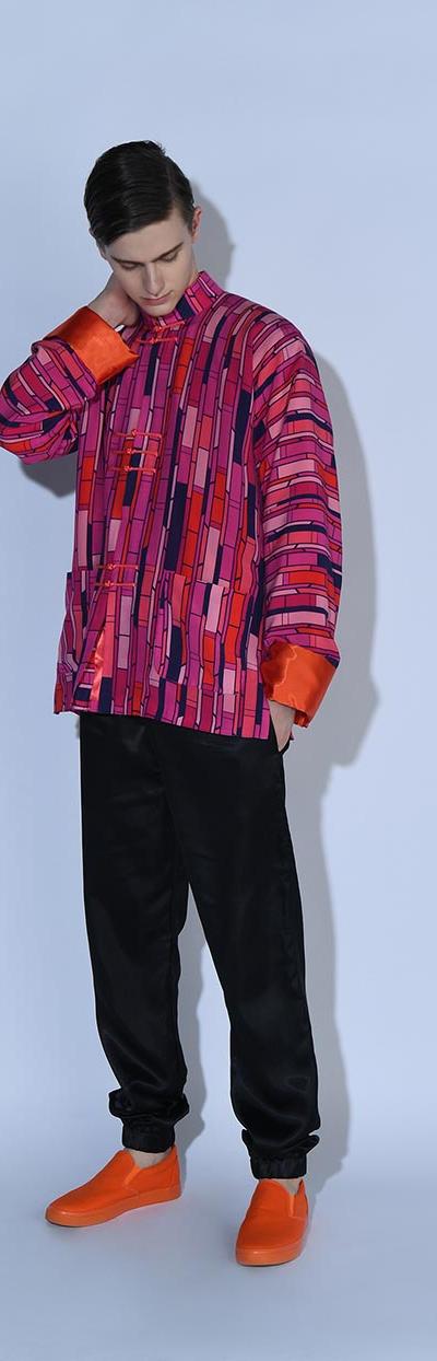 A man wearing a bold pink and purple patterned oversized jacket with black trousers and orange sneakers
