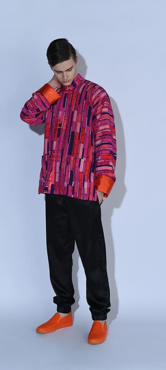 A man wearing a bold pink and purple patterned oversized jacket with black trousers and orange sneakers