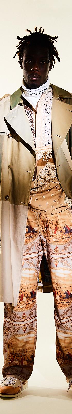 A man wearing a Children of the Discordance layered trench coat with scarf-print patchwork trousers
