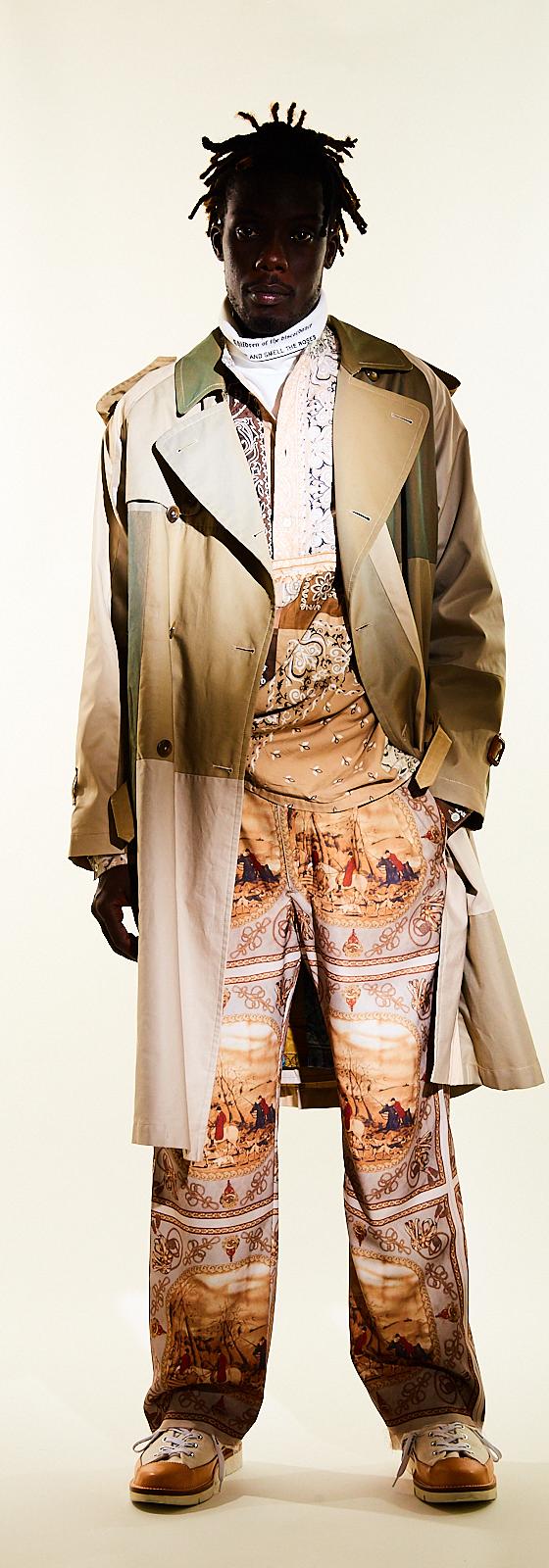 A man wearing a Children of the Discordance layered trench coat with scarf-print patchwork trousers