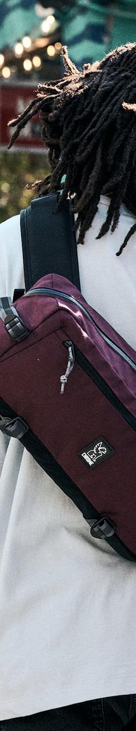 A person wearing a white tee with a burgundy Chrome Industries sling bag across their back on a city street