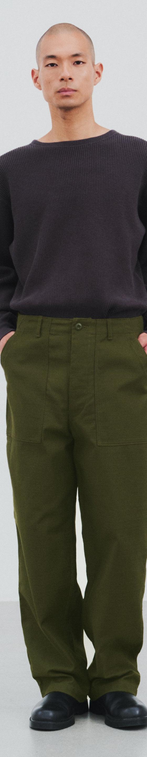 A man wearing a dark brown CIOTA crewneck sweater with olive wide-leg fatigue trousers