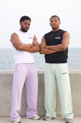 Two men wearing CNTRBND sleeveless tops with lilac and mint sweatpants by the waterfront