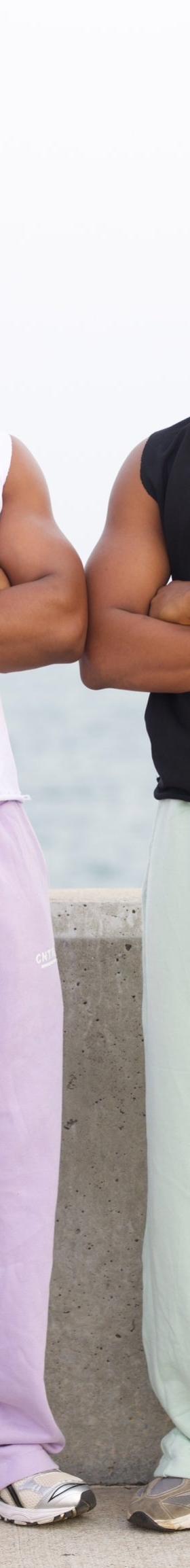 Two men wearing CNTRBND sleeveless tops with lilac and mint sweatpants by the waterfront