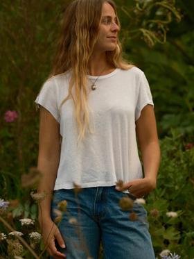 A woman wearing a white cotton tee and blue jeans standing in a wild garden