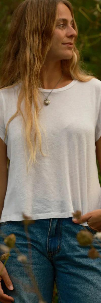 A woman wearing a white cotton tee and blue jeans standing in a wild garden