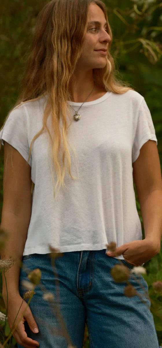 A woman wearing a white cotton tee and blue jeans standing in a wild garden