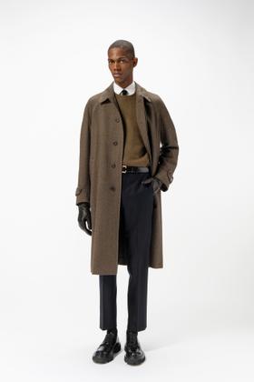 A man wearing a brown herringbone Corneliani overcoat over a khaki sweater and navy trousers