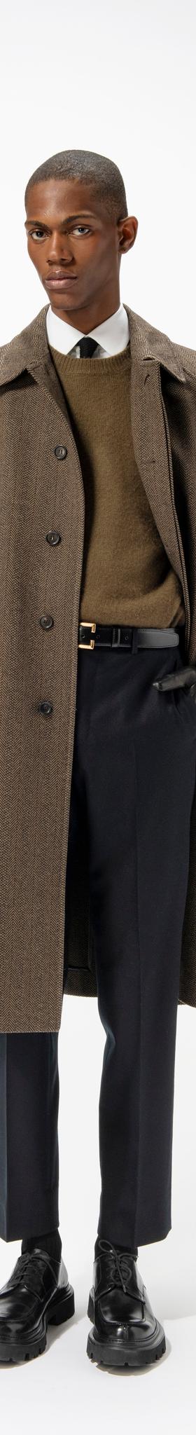 A man wearing a brown herringbone Corneliani overcoat over a khaki sweater and navy trousers
