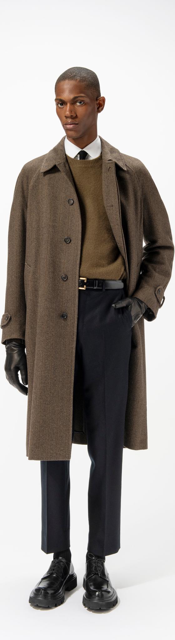 A man wearing a brown herringbone Corneliani overcoat over a khaki sweater and navy trousers