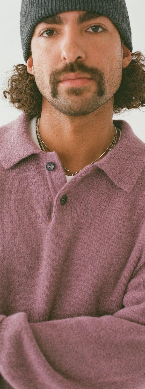 A man wearing a mauve Corridor brushed knit polo sweater and grey beanie