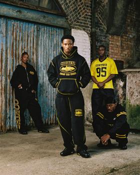 Four models wearing black and yellow Corteiz hoodies, tracksuits and a football jersey in a London warehouse