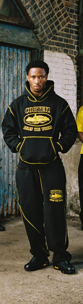 Four models wearing black and yellow Corteiz hoodies, tracksuits and a football jersey in a London warehouse