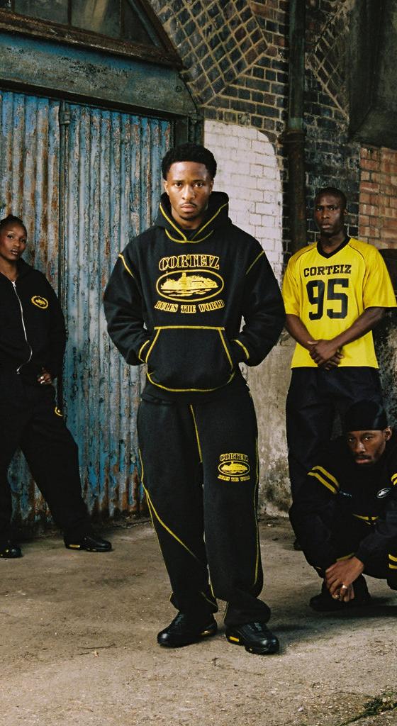 Four models wearing black and yellow Corteiz hoodies, tracksuits and a football jersey in a London warehouse