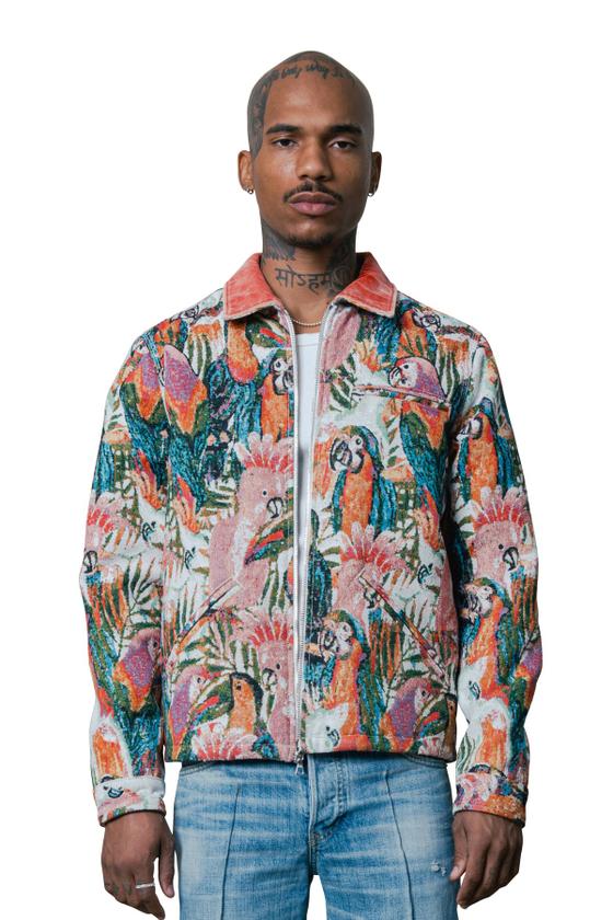 A man wearing a COÛT DE LA LIBERTÉ tropical parrot tapestry zip jacket with light-wash jeans