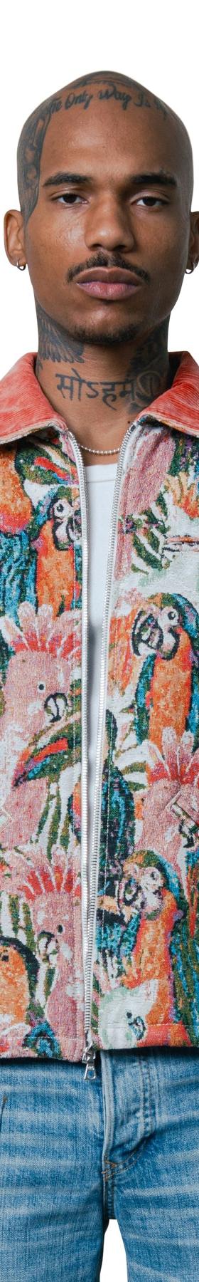 A man wearing a COÛT DE LA LIBERTÉ tropical parrot tapestry zip jacket with light-wash jeans