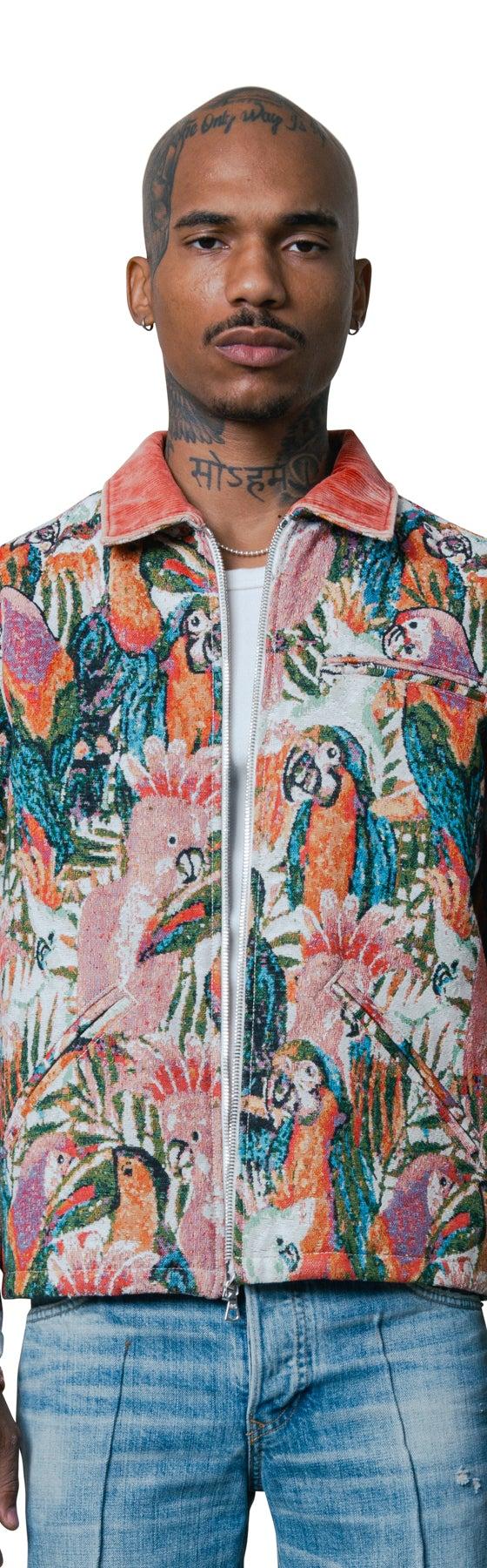A man wearing a COÛT DE LA LIBERTÉ tropical parrot tapestry zip jacket with light-wash jeans