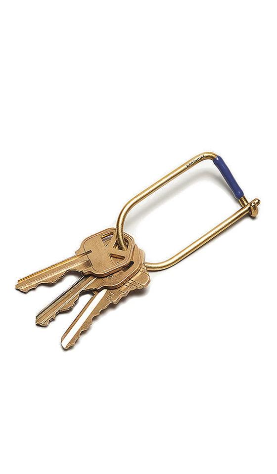 A brass Craighill wilson keyring with blue accent holding three keys on a white background