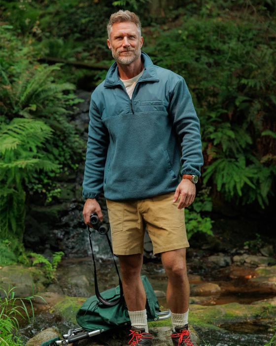 A man wearing a teal Criquet half-zip fleece pullover and khaki shorts