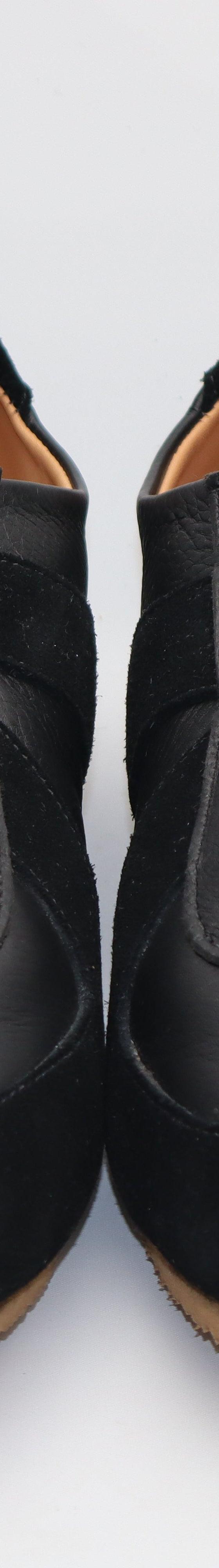 A pair of black leather and suede handmade sneakers on a plain white background