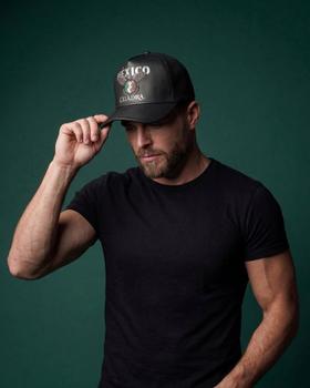 A man wearing a black leather Cuadra México trucker cap and a black t-shirt