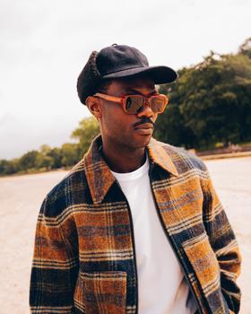 A man wearing tortoiseshell Cubitts sunglasses with a checked wool jacket and cap