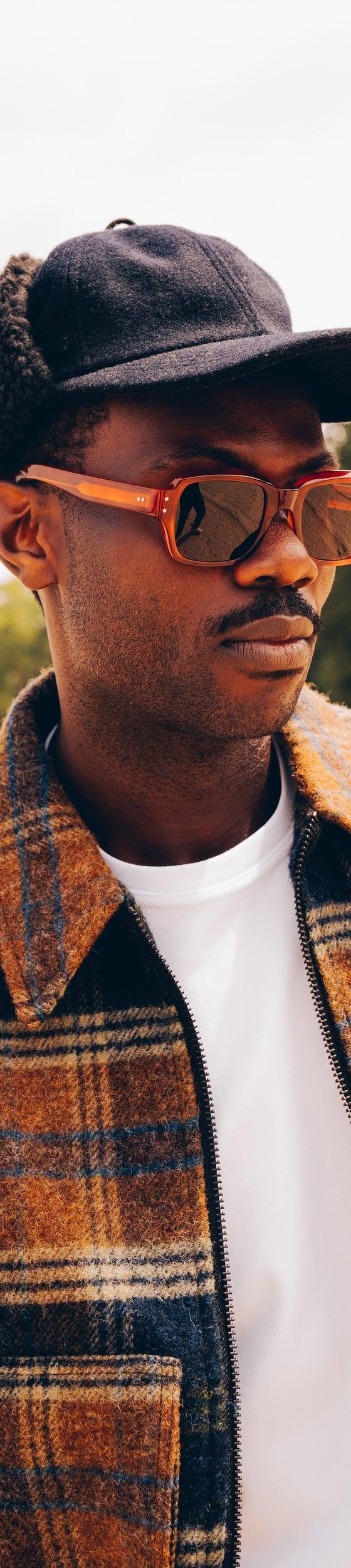 A man wearing tortoiseshell Cubitts sunglasses with a checked wool jacket and cap