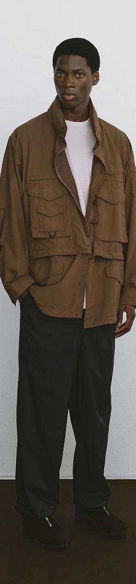 A man wearing a brown DAIWA PIER39 multi-pocket field jacket with black trousers
