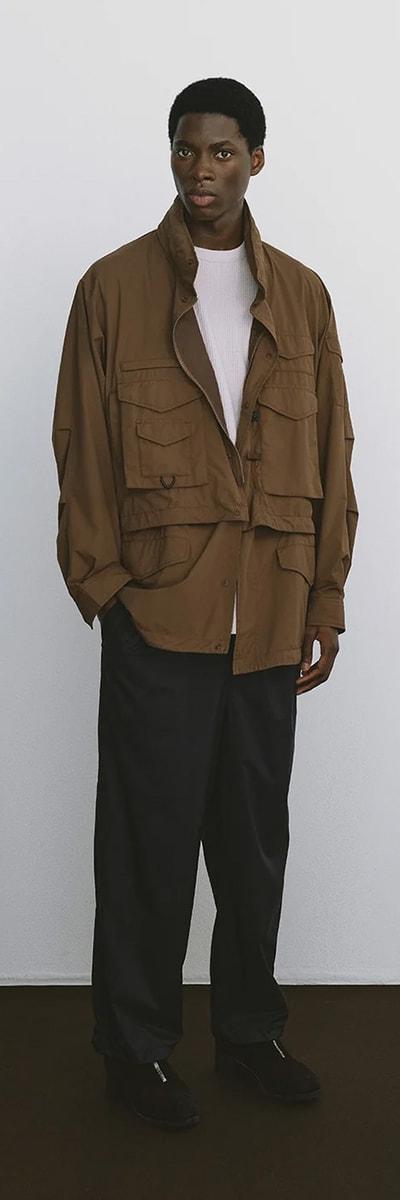 A man wearing a brown DAIWA PIER39 multi-pocket field jacket with black trousers