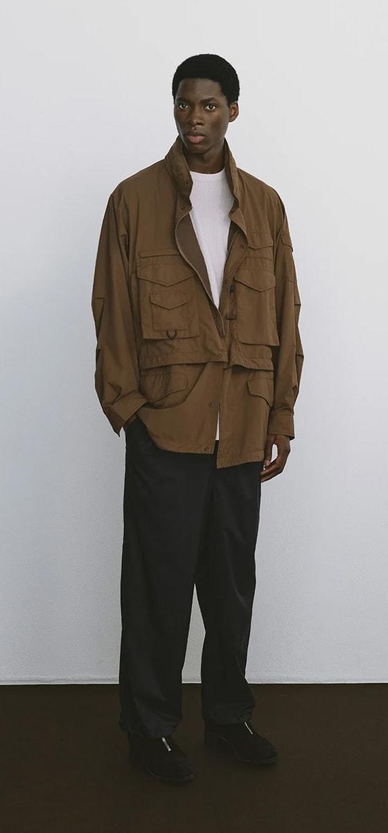 A man wearing a brown DAIWA PIER39 multi-pocket field jacket with black trousers