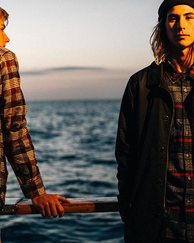 Two men wearing Dark Seas Division plaid flannel shirts and a dark work jacket at sea
