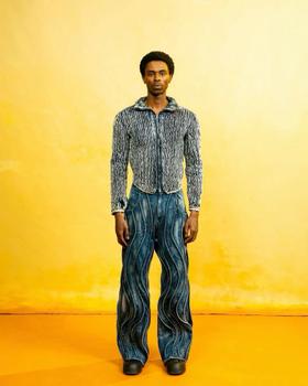 A man wearing a Daveed Baptiste textured denim jacket and swirl-panelled wide-leg jeans