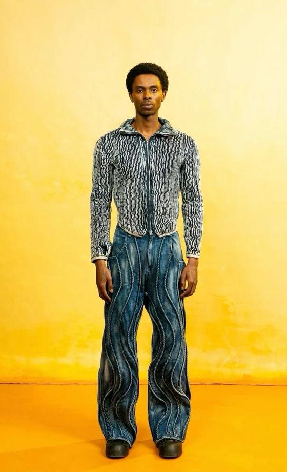 A man wearing a Daveed Baptiste textured denim jacket and swirl-panelled wide-leg jeans