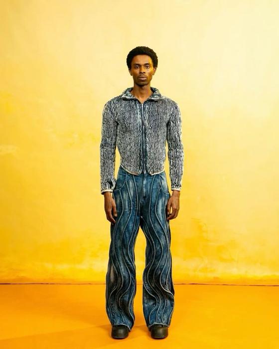 A man wearing a Daveed Baptiste textured denim jacket and swirl-panelled wide-leg jeans
